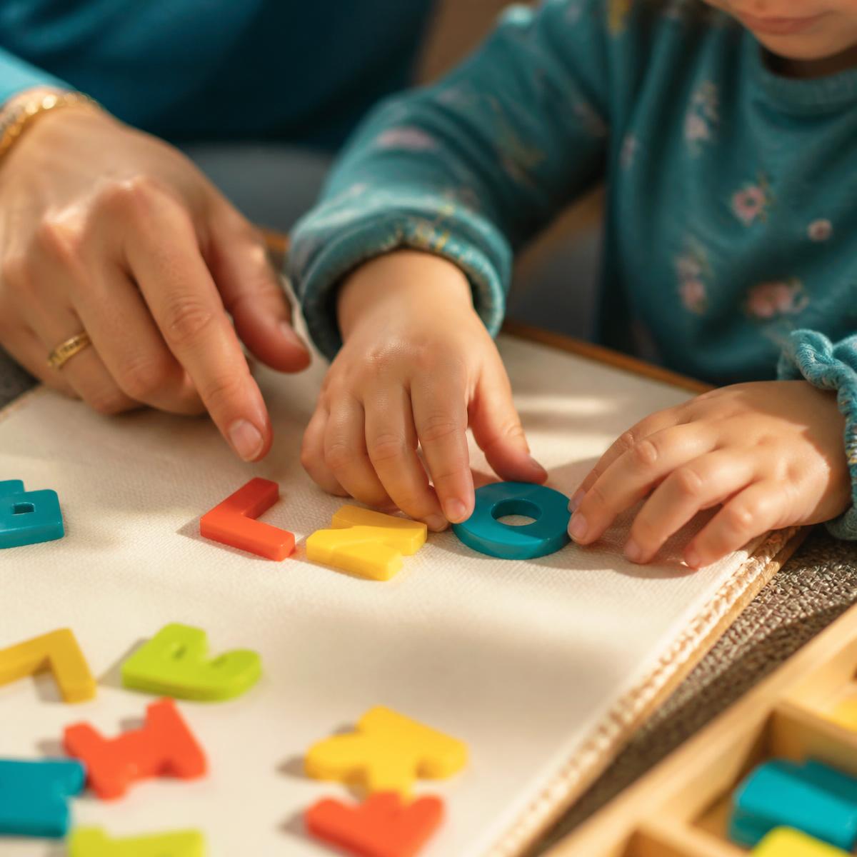 A child moving colorful letter tiles to build a word with a tutor guiding